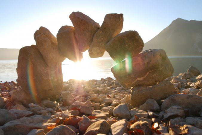 LandArt: Ein Torbogen aus großen Steinen vor einem See gegen die Sonne fotografiert