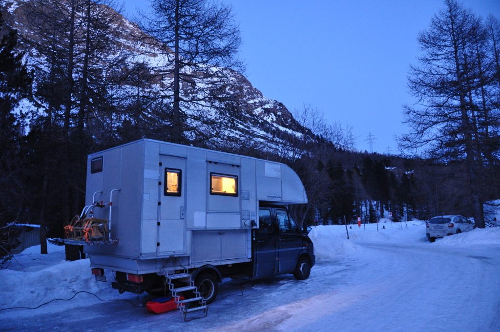 Wohnmobil mit Individualaufbau in Abendstimmung am verschneiten Campingplatz Morteratsch.